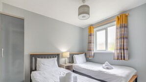 Une chambre d’hôtel avec deux lits simples, une armoire, une table de chevet avec une lampe et une fenêtre avec des rideaux.