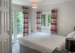 A bedroom with a bed, a bedside table, a lamp, and a view of the outdoors through a window.