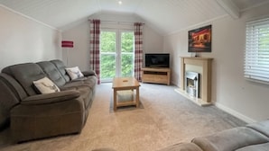 A living room with a sofa, a coffee table, a fireplace, and a television. - 3 bedroom accommodation in Milnthorpe (Milnthorpe)