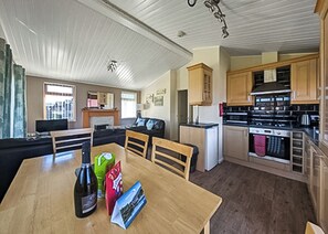 A living room with a sofa, a dining table with chairs, a kitchen with wooden cabinets, and a refrigerator.
