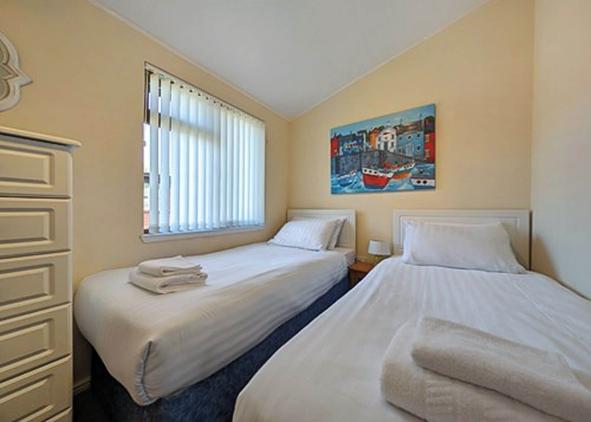 A room with two beds, a window with blinds, a painting on the wall, and a dresser.
