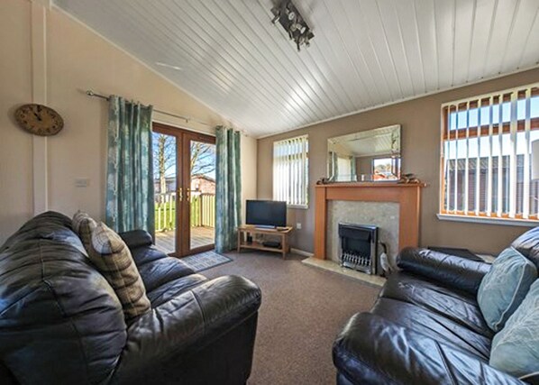A living room with two leather sofas, a television, a fireplace, and a sliding glass door leading to a patio.