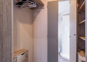 Um closet amplo com um banco de madeira, cabideiro e porta de vidro do chuveiro.
