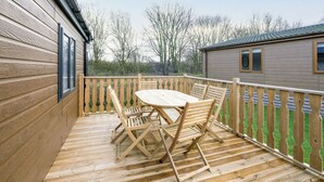 A wooden deck with a table and chairs, a wooden fence, and a building in the background.