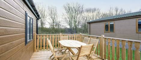 A wooden deck with a table and chairs, a wooden fence, and a building in the background.