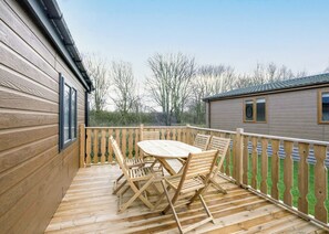 A wooden deck with a table and chairs, a wooden fence, and a building in the background.