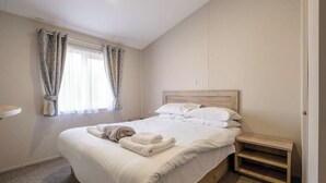 A bedroom with a bed, a bedside table, a window with curtains, and a wall-mounted light.