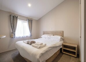 Quarto com cama, mesa de cabeceira, janela com cortinas e luminária na parede.