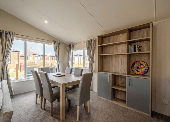 A room with a dining table, chairs, a bookshelf, and a dartboard.