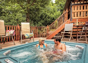 Ein Whirlpool mit zwei Personen, umgeben von Holzliegen und einer Holztreppe.