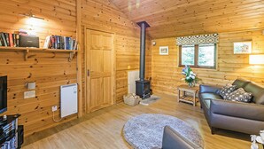 A cozy cabin interior with wooden walls, a fireplace, a sofa, and a bookshelf. - 1 bedroom accommodation in Harrogate (Harrogate)