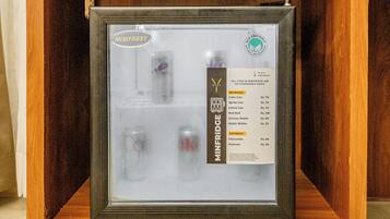 Un minibár con puerta de vidrio, que contiene un refrigerador pequeño y una variedad de bebidas y aperitivos.