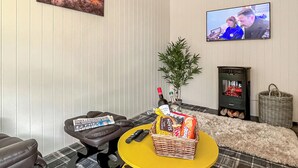 A room with a television, a sofa, a table with snacks, a chair, and a fireplace.