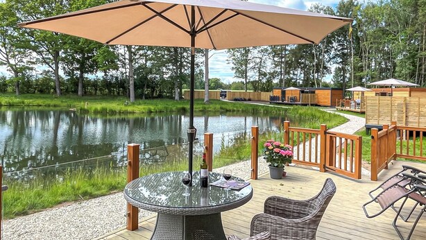 A deck with a table and chairs, a wooden fence, and a body of water in the background.