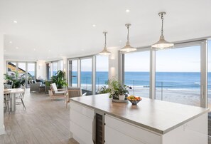 A modern kitchen with large windows overlooking the ocean, a dining area with a view, and a spacious living area with a sofa and plants.