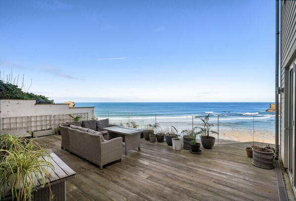 A wooden deck with outdoor furniture, potted plants, and a view of the ocean.