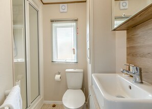 Une salle de bain équipée de toilettes, d’une douche, d’un lavabo et d’une fenêtre avec des stores.