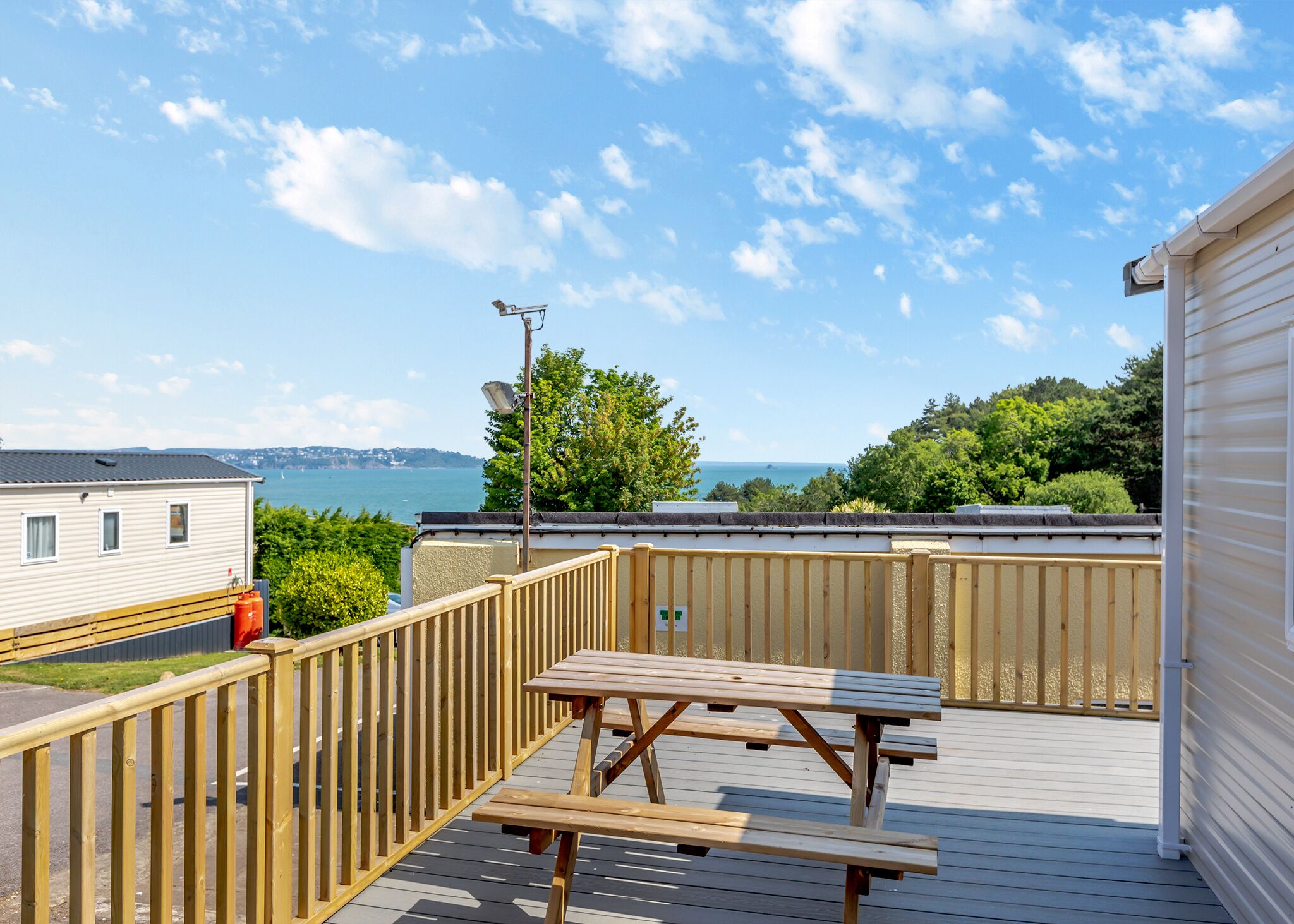 Eine Terrasse mit Picknicktischen mit Blick auf ein Gewässer, ein weißes Gebäude und Meerblick.