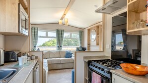 A compact kitchen with a stove, sink, and a dining area with a sofa. - Gold 2 bedroom Caravan (Brixham, Torbay)