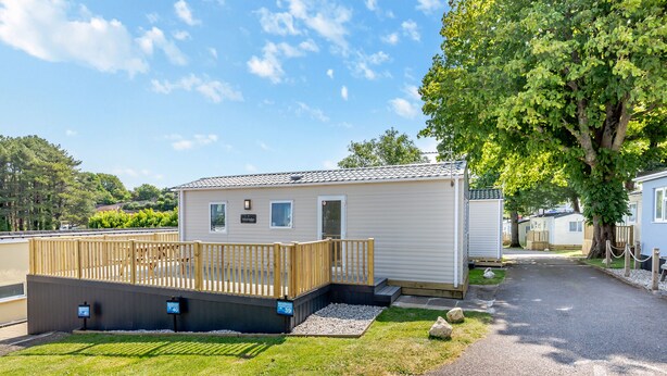 A mobile home with a deck, a covered porch, and a gravel driveway. - Gold 2 bedroom Caravan (Brixham, Torbay)