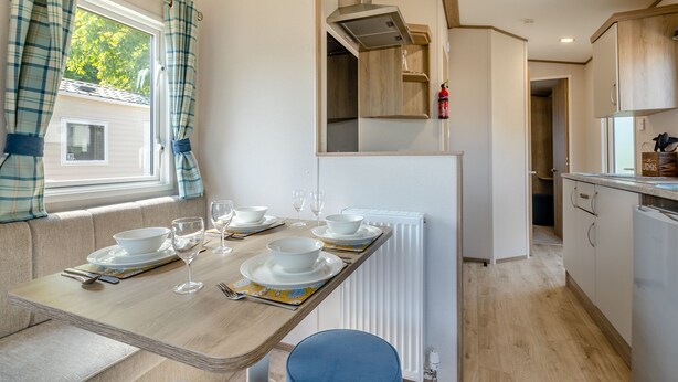 A compact kitchen with a dining area, a radiator, and a view of the outside. - Gold 2 bedroom Caravan (Brixham, Torbay)