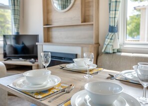 Une table à manger dressée avec de l’assiette blanche, des bols et des verres à vin, avec un téléviseur en arrière-plan.