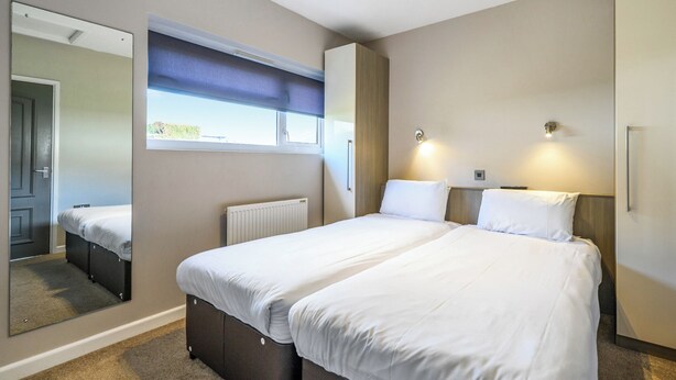 A hotel room with a large bed, a mirror, a window with a view, a radiator, and a wardrobe. - Shoreline Apartment 1 (Pets Welcome) (Woolacombe)