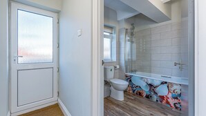 A bathroom with a toilet, shower, and a tiled wall with a decorative pattern. - Shoreline Apartment 3 (Pets Welcome) (Woolacombe)