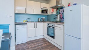 A compact kitchen with white cabinets, a microwave, a stove, and a refrigerator. - Shoreline Apartment 3 (Pets Welcome) (Woolacombe)