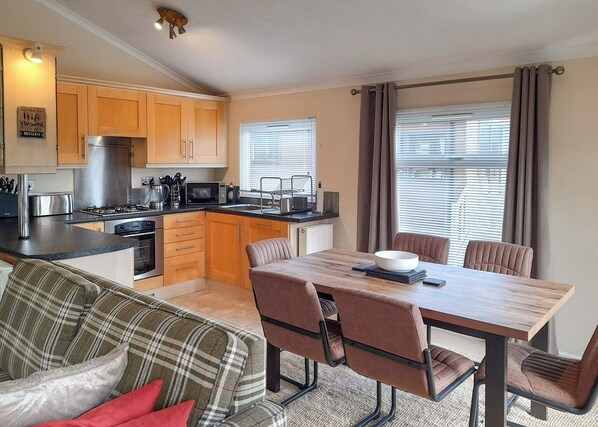 A modern kitchen with wooden cabinets, a dining table with chairs, and a sofa with plaid cushions.