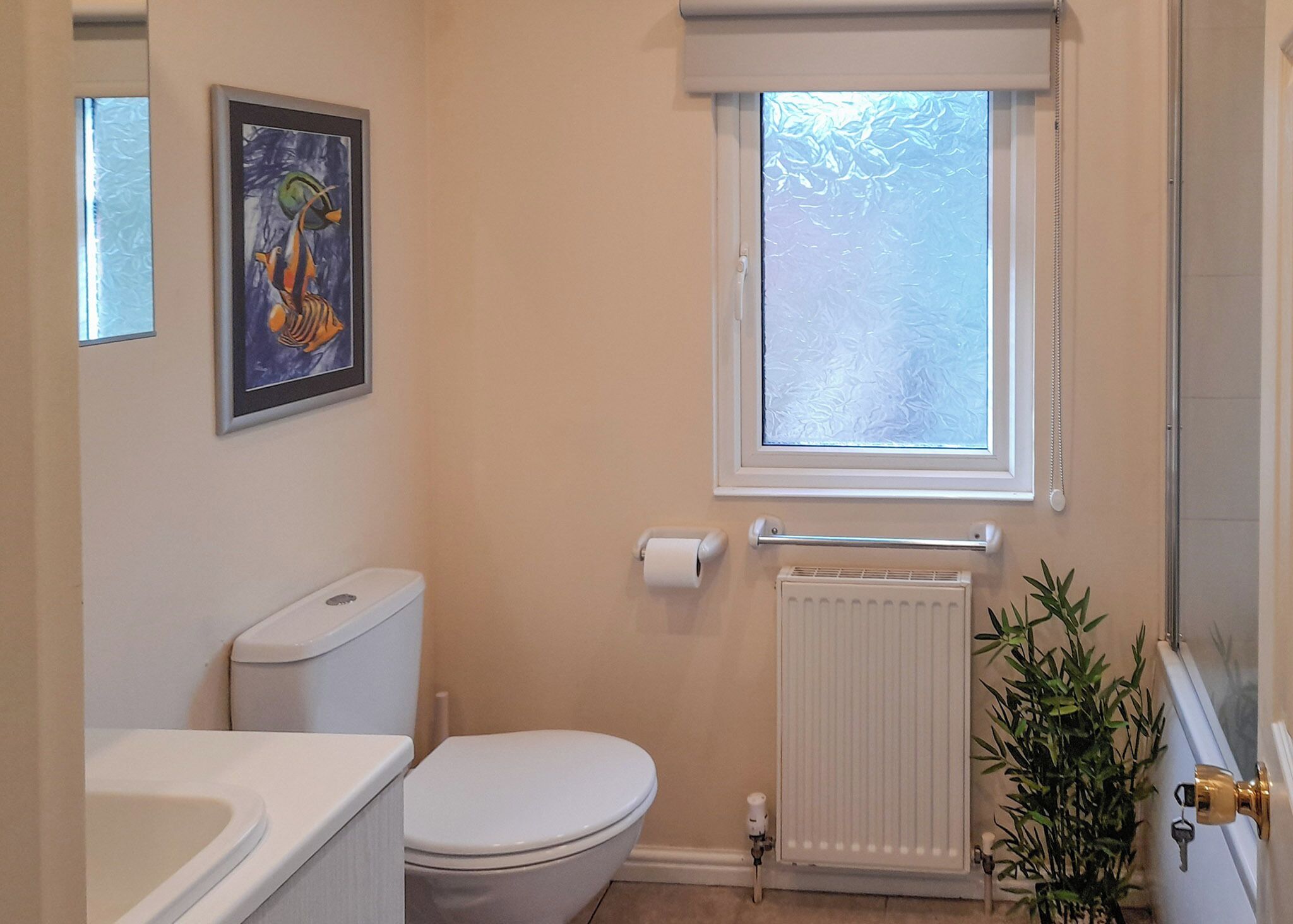 Une salle de bain avec des toilettes, un radiateur, une fenêtre et un tableau encadré au mur.