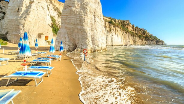 Une plage bordée de falaises blanches, sous un ciel bleu azur, et où le sable scintille sous le soleil.