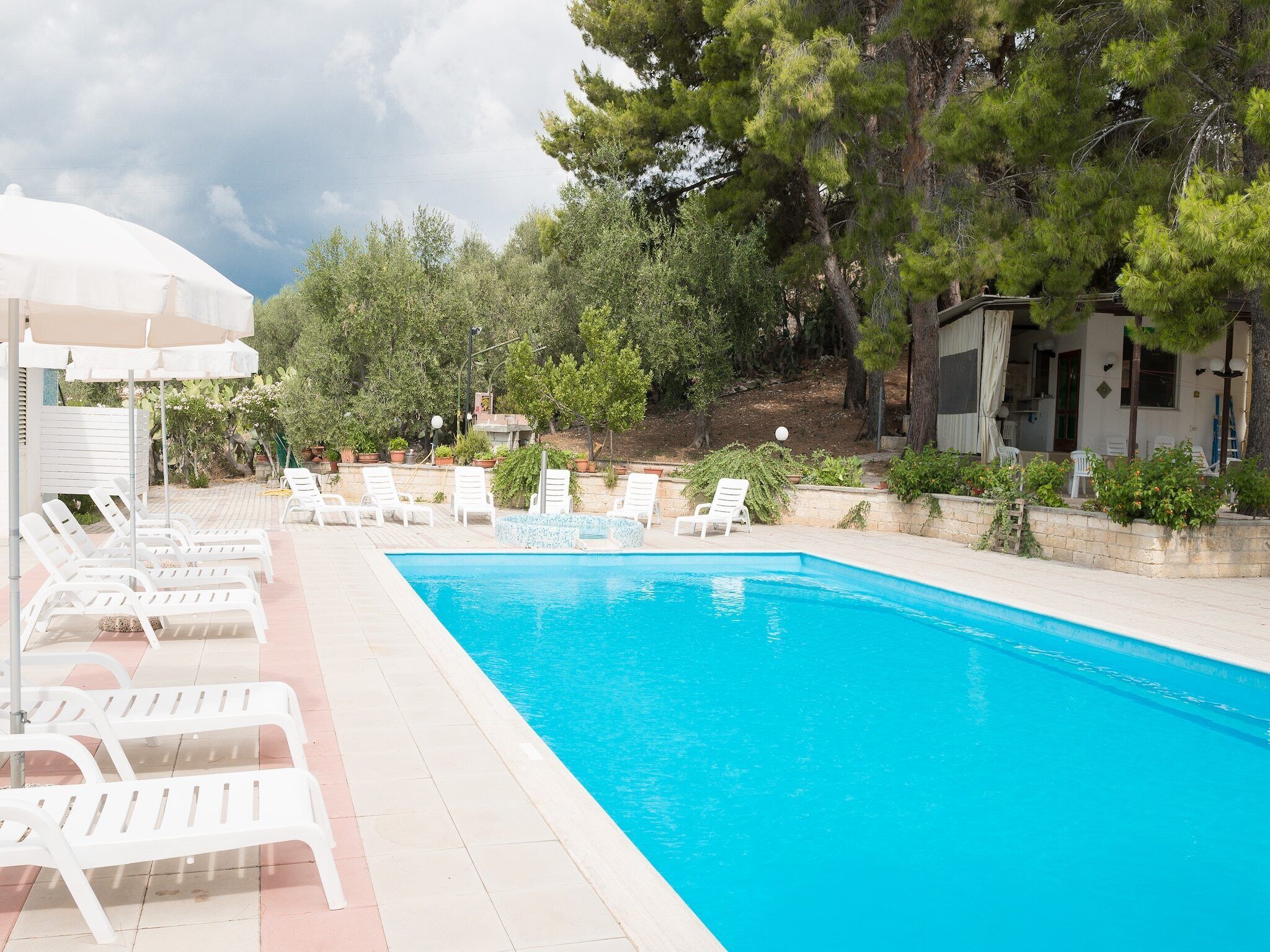 Une piscine entourée de chaises longues blanches et d’un espace abrité avec des parasols.