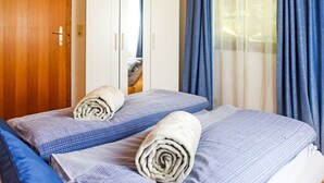 Ein Hotelzimmer mit zwei Betten, jedes mit einem zusammengerollten Handtuch und einer blau karierten Bettdecke.