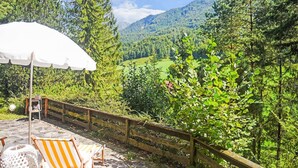 Eine Terrasse mit Tisch und Stühlen, ein Holzzaun und Blick auf ein bewaldetes Tal mit Bergen im Hintergrund.