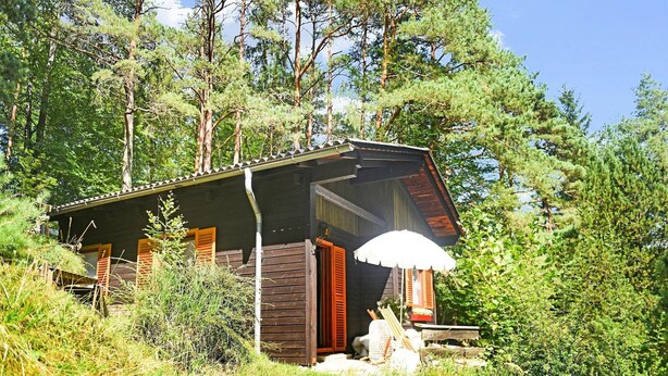 Eine Holzhütte mit einer Veranda und einer Bank, sowie einem weißen Sonnenschirm.