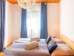 Une chambre avec un plafond en bois, un lit avec des serviettes roulées, des rideaux bleus et une porte blanche.