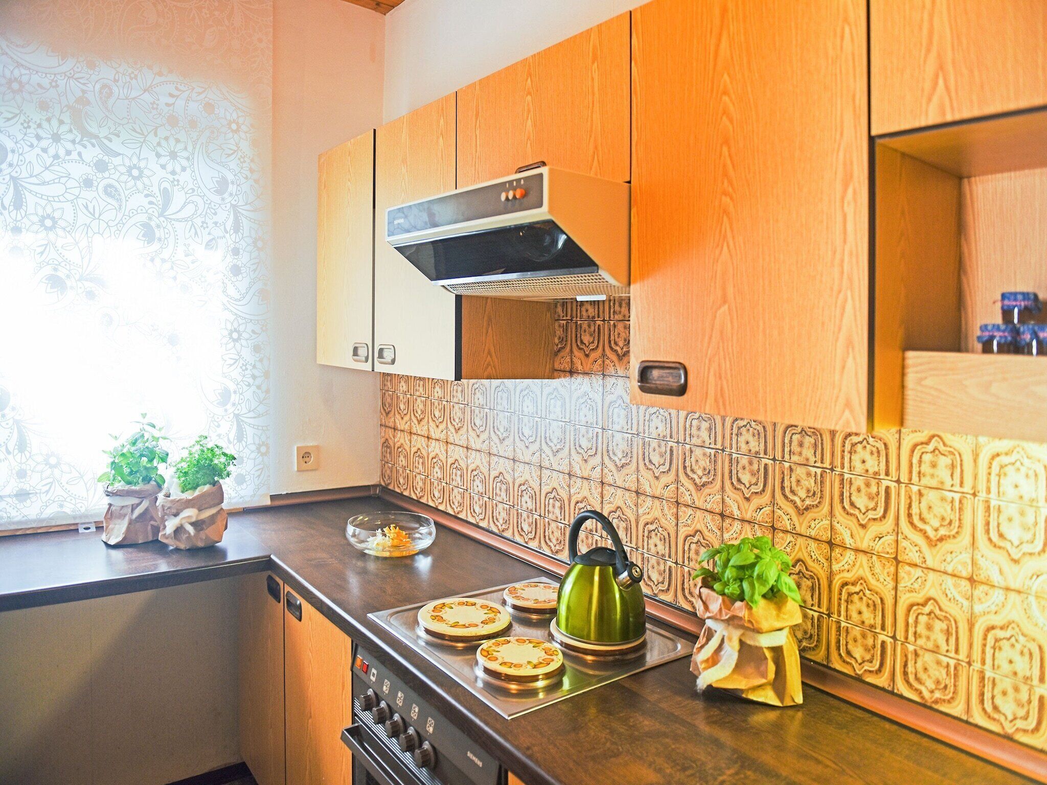 A kitchen with wooden cabinets, patterned backsplash, and a stove with a kettle.