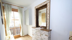 A room with a stone fireplace, a wooden bench, a small table with a candle, and a window with curtains.