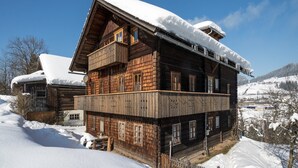 A wooden chalet with a balcony, surrounded by snow-covered hills.