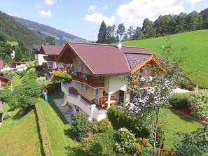 A multi-story house with a red-tiled roof, a balcony with wooden railings, and a well-maintained garden with various plants and a small play area. - Apartment in Kleinarl near Ski Amadé (Kleinarl)