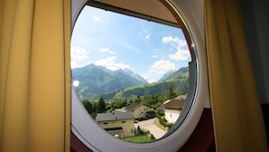Une fenêtre donnant sur un paysage montagneux, des maisons et un ciel dégagé.