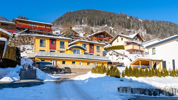 Un village enneigé aux bâtiments aux couleurs vives, un ciel dégagé et une montagne en arrière-plan.