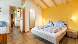 A bedroom with a wooden bed, a bedside table, and a small drawer unit. There is a wooden ceiling and a yellow wall. - Apartment in Hollersbach near Kitzbühel ski lift (Hollersbach im Pinzgau)