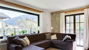 Un salon moderne avec un canapé d’angle, de grandes fenêtres offrant une vue sur les montagnes et un plafond en bois.
