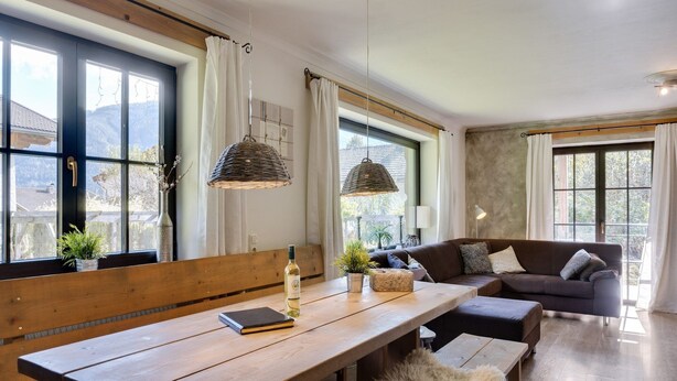 Un salon chaleureux avec un banc en bois, un canapé et une table à manger sur laquelle se trouvent une bouteille et un livre.