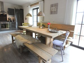 A modern kitchen with a wooden table, bench, and chairs, a refrigerator, and a window with curtains. - Chalet in Leogang near Ski Slopes (Leogang)