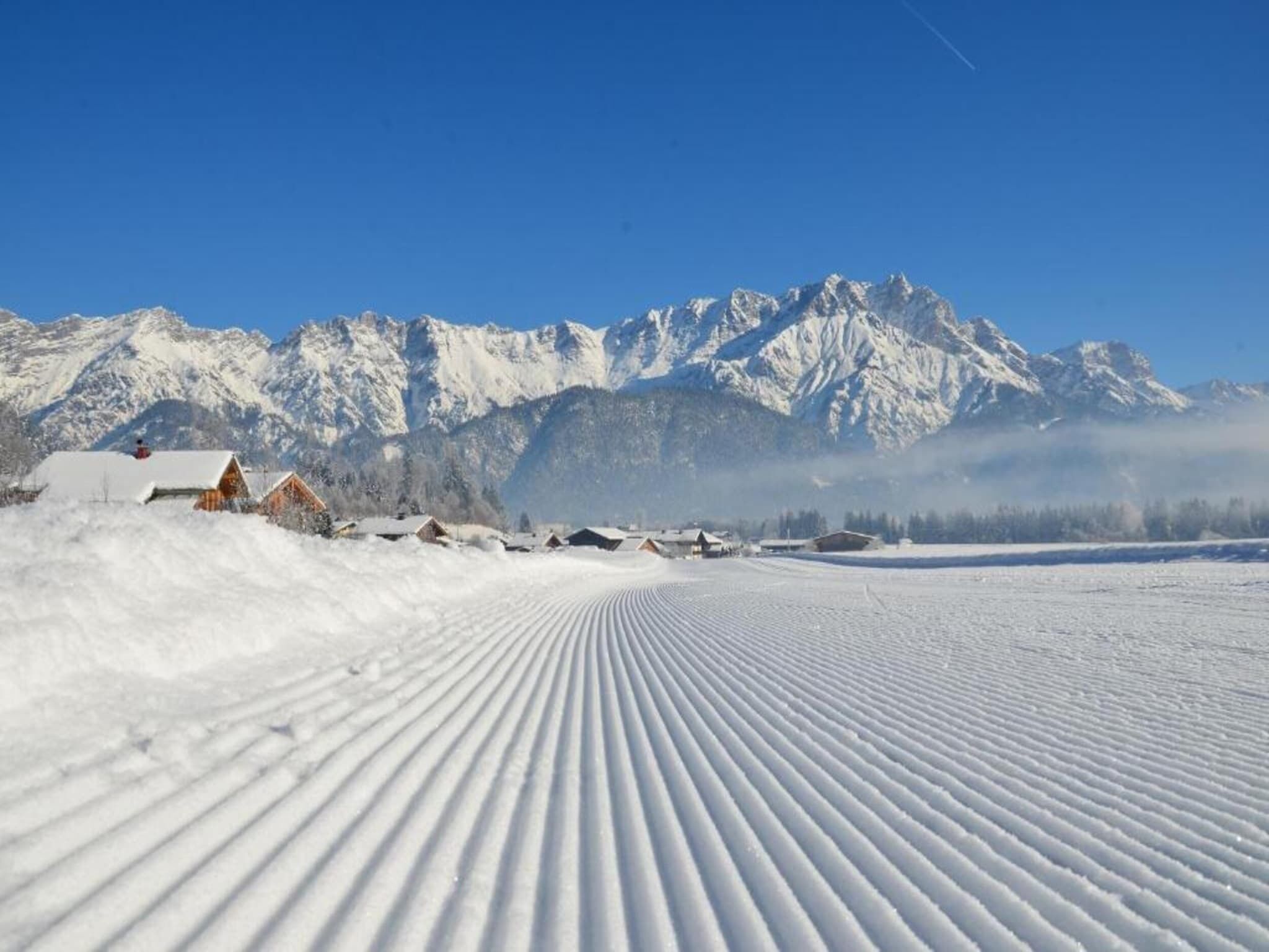 Eine verschneite Landschaft mit einem Bergpanorama im Hintergrund und blauem Himmel.
