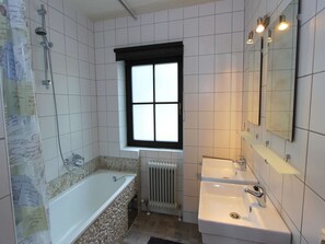Ein Badezimmer mit einer Badewanne, zwei Waschbecken, einem Fenster und einer Heizung.