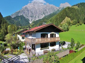 Un chalet doté d’un balcon, entouré d’un paysage verdoyant et de montagnes.